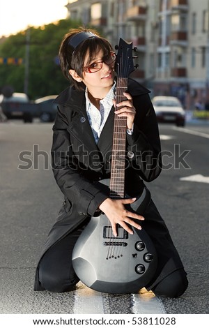 White brunette chick with black electric guitar sitting on the road