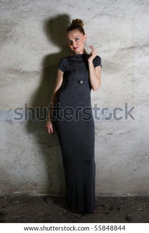 Girl in long grey dress with a cigarette in her hands standing near dirty wall