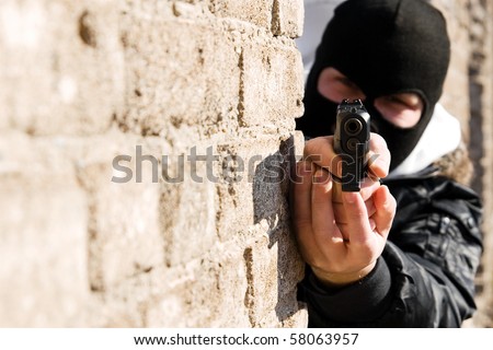 Armed man in black mask pointing a gun in camera