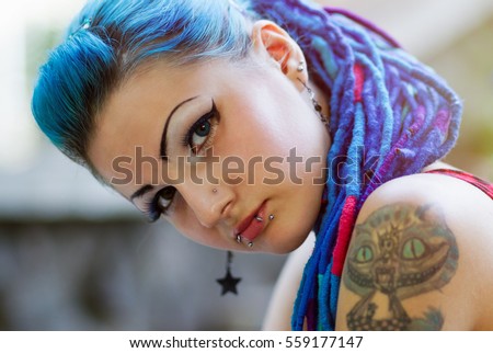 Portrait of cool young girl with blue braided hair,lip piercing on her face,tattoo on her shoulder.Punk white teen girl with body modification.Stylish youth fashion,fashionable chick.Cool hair model