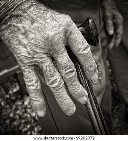 Hand of old man with arthritis supported with walking stick in black and white