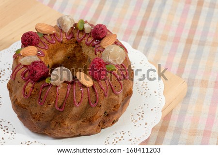 Gugelhupf marble Bundt cake, filled with dried blackcurrant and chestnut paste, garnished with blackcurrant icing, marron glace, whole almonds, freeze-dried raspberry, pistachios, and silver dragees.