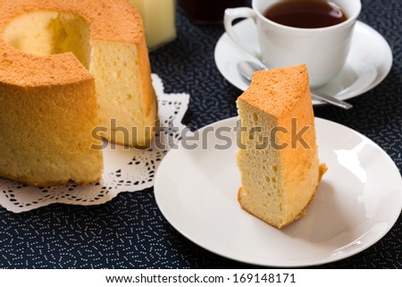 Chiffon cake with characteristic hole in the center from an ungreased tube pan. The cake is made with vegetable oil, eggs, sugar, flour, and flavorings. Served with raspberry jam, and a cup of tea.