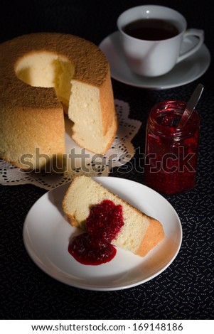 Chiffon cake with characteristic hole in the center from an ungreased tube pan. The cake is made with vegetable oil, eggs, sugar, flour, and flavorings. Served with raspberry jam, and a cup of tea.