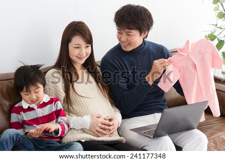 Happy expecting family of three shopping on a laptop. Father shows long-sleeve bodysuits of pink color.
