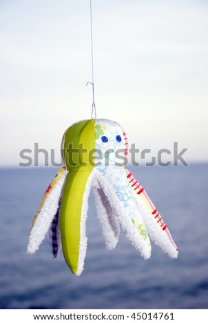 Soft toy octopus handmade from cotton and terry cloth with the sea and the sky in the background.