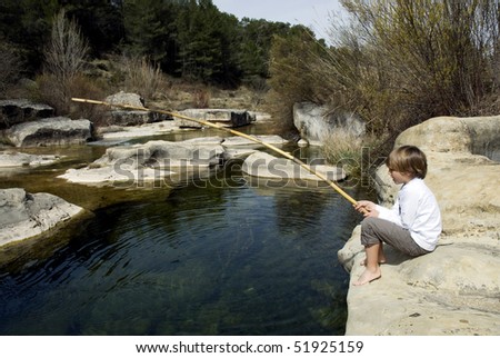 Child sitting at the shore of a river fishing with a bamboo rod