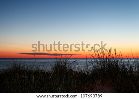 Dunes with grass silhouetted by a summer sunset over Lake Michigan.