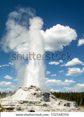 Hot water gushes into the air against a cloudy deep blue sky from Castle Geyser in the Upper Geyser Basin of Yellowstone National Park, Wyoming, USA. Castle Geyser is not far from Old Faithful Geyser.