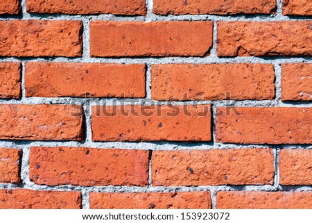 An old wall is constructed of orange red clay bricks showing a rustic and worn texture.
