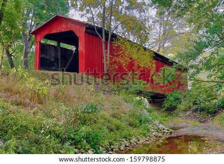 A red covered bridge crosses a creek in rural Indiana. Shot at the Cornstalk Covered Bridge in Putnam County.