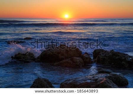 The sun rises over the Atlantic Ocean with waves breaking on a Florida beach covered with coquina stone.