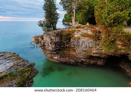 Early morning long exposure photo at Door County, Wisconsin\'s Cave Point, on Lake Michigan, reveals rocky cliffs, colorful waters, and a cloudy sky.