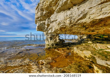A rock arch window has been eroded by the waves at Door County, Wisconsin\'s Cave Point  with a cloudy blue sky.