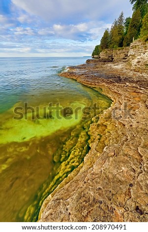 The rocky and rugged coastline of Door County, Wisconsin\'s Cave Point displays colorful pools under a cloudy blue morning sky.