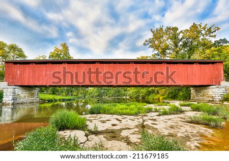 The Cataract Falls Covered Bridge Crosses Indiana\'s Mill Creek with a cloudy blue evening sky above.