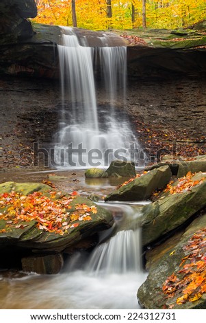 Ohio\'s Blue Hen Falls in Cuyahoga Valley National Park spills over a cliff and boulders covered with colorful fall leaves.