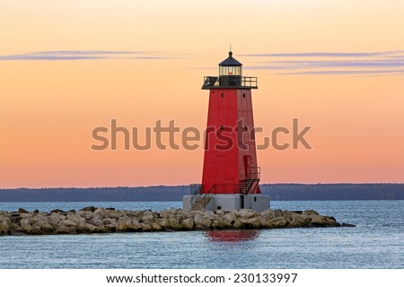 The sky glows with color as the sun rises on the red lighthouse at Manistique on the Lake Michigan Coast of Michigan\'s Upper Peninsula.