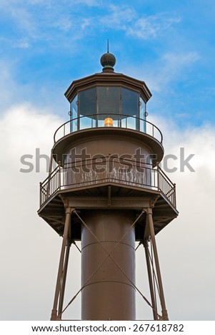 The beacons shines in the lantern room of  Florida\'s Sanibel Island LIghthouse backed by a cloudy blue sky.