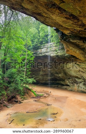 A slender waterfall pours over the edge of Ash Cave in Ohio\'s Hocking Hills State Park. At 90 feet high and 700 feet wide, Ash Cave, eroded from Blackhand sandstone, is Ohio\'s largest recess cave.