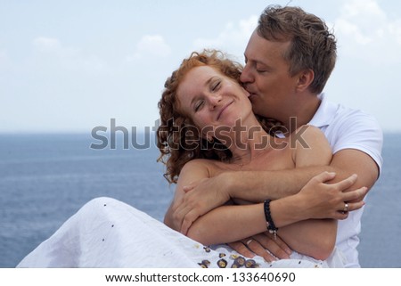 Happy man hugging his wife and kissing her ear at beach