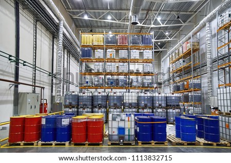 Blue and red oil drums and plastic container on pallets in a warehouse on metal shelving. Handling and storing industrial lubricants. Hazardous Material Storage