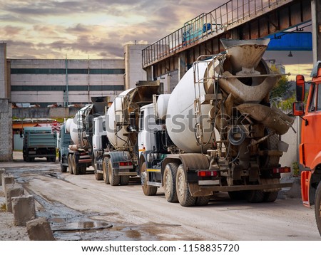 Heavy mixer concrete trucks waiting for to be loaded on the concrete mixing and batching factory. Deficiency of concrete and sand formed a queue for loading at the building materials factory.