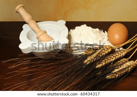 Eggs, flour, wheat ears and mortar on wood table