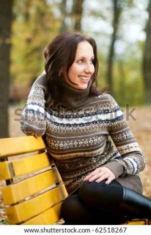 Young woman sitting on bench and smiling in autumn park