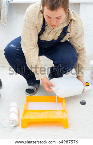 young worker pouring paint from a large bucket