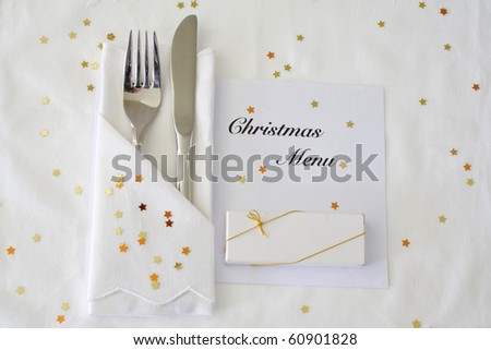 Knife and fork with Christmas menu on white linen with gold stars