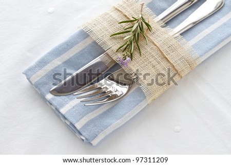 Knife and fork with a blue and white striped napkin and rosemary