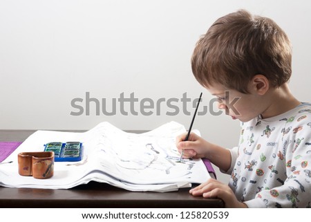 Kid drawing with water colors on table