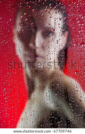 Beautiful slim girl behind wet glass