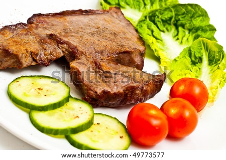 Juicy stake with salad, tomatoes, cucumbers on a plate, isolated on a white background