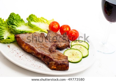 Juicy stake, glass of wine and salad, tomatoes, cucumbers on a plate, isolated on a white background