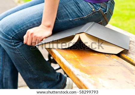 opened book on a wooden park bench next to a woman