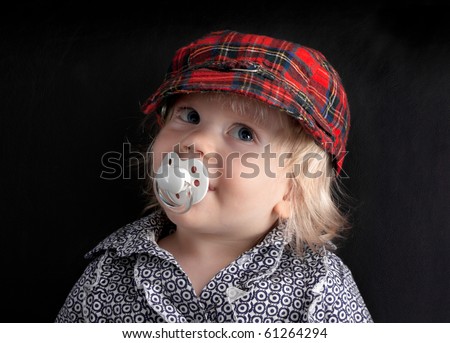 Cute baby in a cap and with a pacifier on a black background