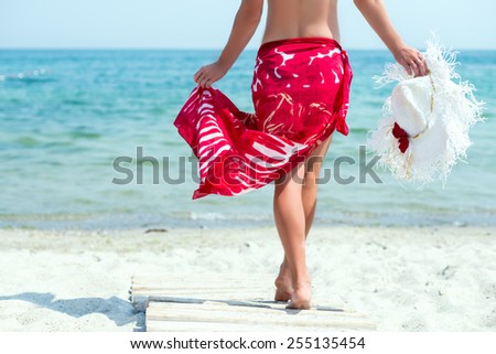 Beautiful woman with white hat walks at the sea side in red dress