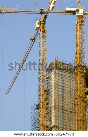 High rise building under construction with two tower cranes isolated against a blue sky