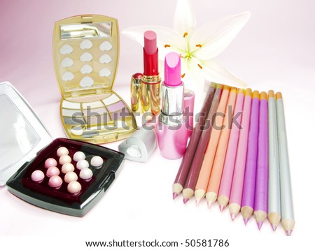 lipsticks eye shadows pencils lip gloss and lily on background