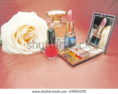 red lipstick powder yellow rose eye shadow and perfume on satin cloth background