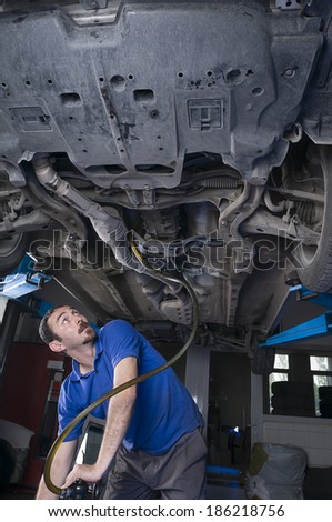 Adult Turkish mechanic draining engine oil at auto repair shop for oil change
