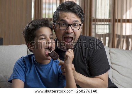 Father and son enjoying chocolate-coated blocks of ice cream on stick.