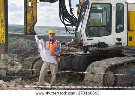 Mechanic engineer checking road plans in front of drilling pile foundation.