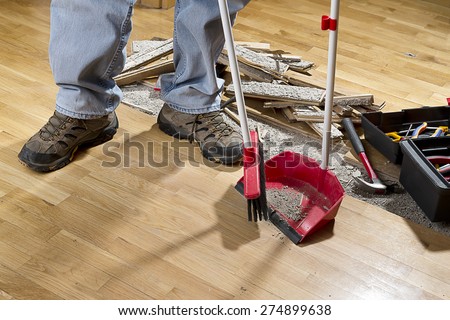 An unrecognizable person with a broom sweeping floor into dustpan.
