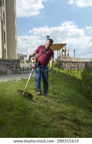 Vertical image of gardener mowing lawn with string lawn trimmer.