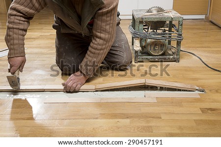 Manual worker fixing wooden floor ruined from moisture and water leak.