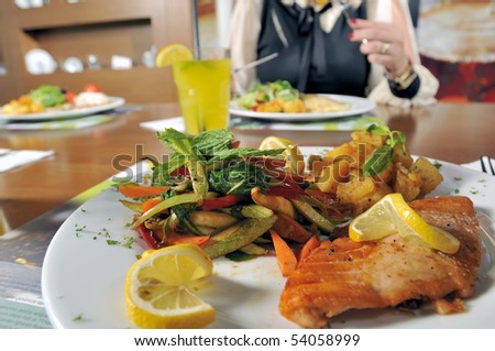 Closeup of grilled salmon fillet with background person at a restaurant.