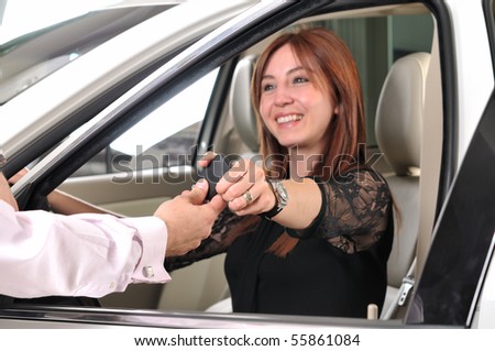 Car dealer giving keys of a new car to happy red head customer - a series of BUYING A NEW CAR images.